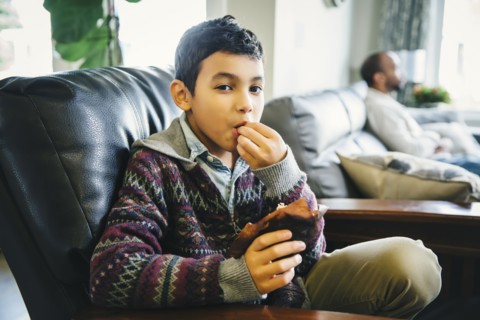 Mixed race boy eating in armchair