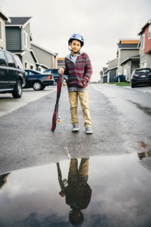 Mixed race boy with skateboard reflected in puddle