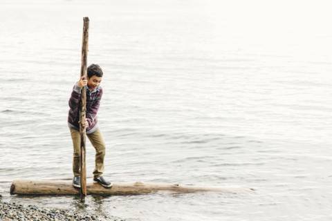 Mixed race boy playing on log in lake