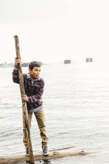 Mixed race boy playing on log in lake
