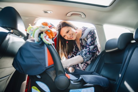 Hispanic mother fastening car seat in car