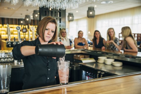 Caucasian bartender pouring cocktail from mixer into glass