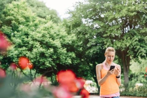 Caucasian woman using cell phone and earbuds outdoors