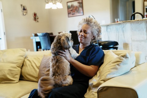 Black woman sitting on sofa playing with dog