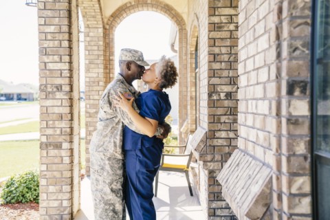 Black soldier kissing wife on front stoop