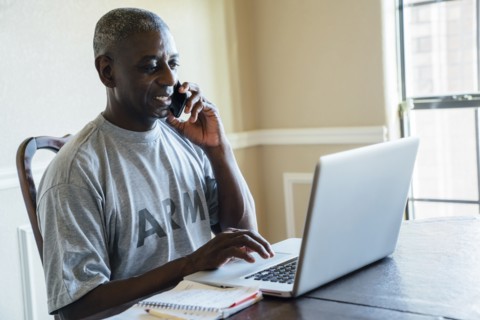 Black man using laptop and cell phone at table