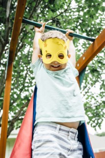 Caucasian boy wearing superhero costume hanging on monkey bars
