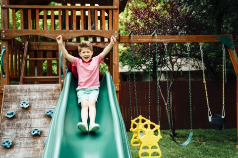 Caucasian boy sliding on backyard playground slide