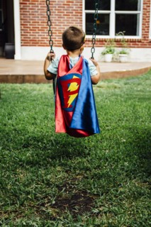 Caucasian boy wearing superhero costume on swing