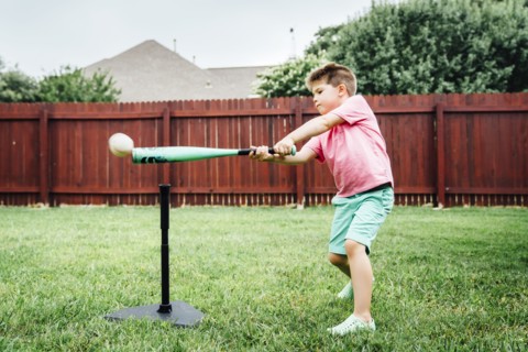 Caucasian boy hitting baseball off tee in backyard