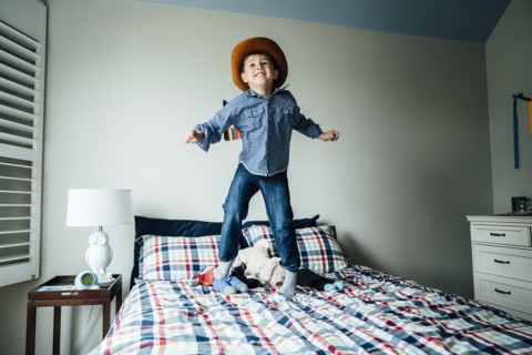 Caucasian boy wearing cowboy costume jumping on bed