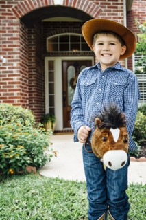 Caucasian boy wearing cowboy costume riding toy horse