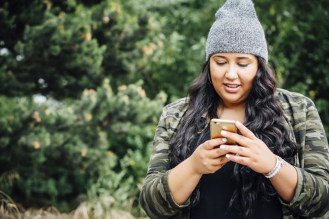 Mixed Race woman texting on cell phone in forest