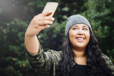 Mixed Race woman posing for cell phone selfie in forest