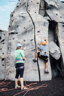 Woman holding rope for man climbing rock climbing wall