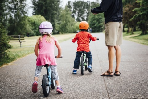 Father watching daughter and son riding bicycles