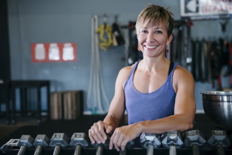 Smiling Caucasian woman leaning on rack in gymnasium