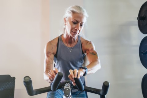 Caucasian woman riding stationary bicycle checking smart watch