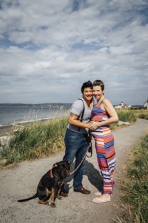Portrait of pregnant lesbian couple with dog hugging at waterfront