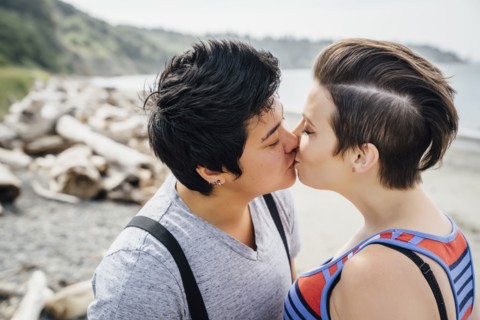 Pregnant lesbian couple kissing on beach