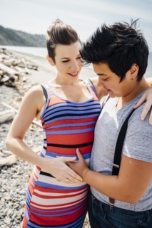 Pregnant lesbian couple hugging on beach