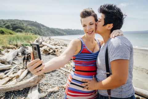 Pregnant lesbian couple posing for cell phone selfie on beach