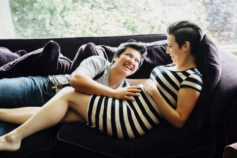 Pregnant lesbian couple cuddling on sofa