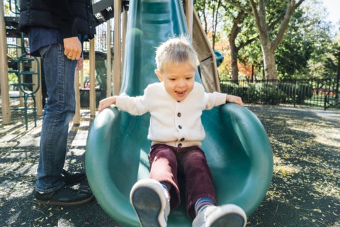 Mixed Race father watching son on playground slide