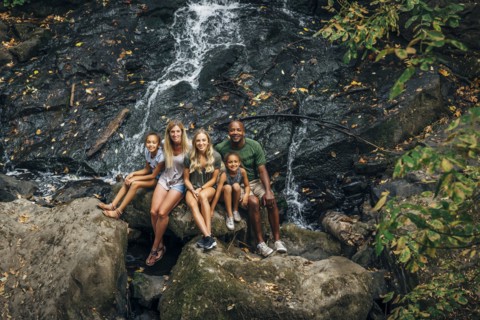 Multi-ethnic family posing on rock near waterfall