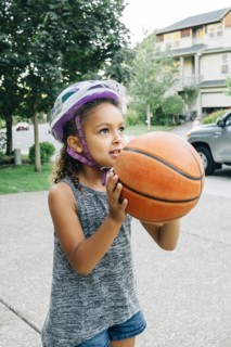 Mixed Race girl wearing helmet playing basketball in driveway