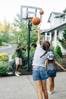 Father and daughters playing basketball in driveway