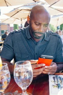 Black man sitting at restaurant table texting on cell phone