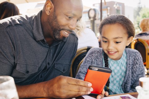 Father and daughter sitting at restaurant table texting on cell phone