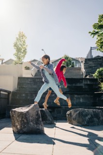 Mixed Race sisters jumping on rocks