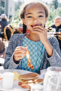Smiling Mixed Race girl eating breakfast at restaurant