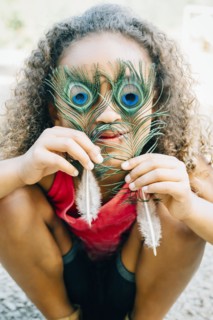 Mixed Race girl covering eyes with peacock feathers