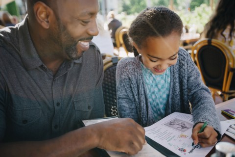Father watching daughter coloring with crayon in restaurant