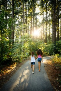 Mixed Race sisters holding hands walking on forest path