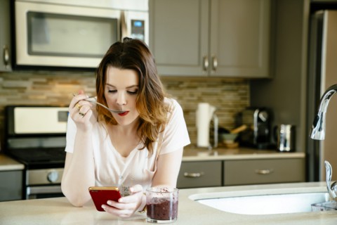 Woman eating smoothie and texting on cell phone