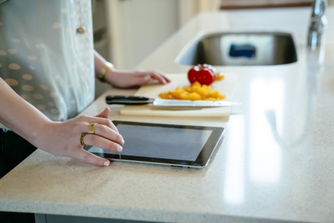 Woman using digital tablet and chopping food in domestic kitchen