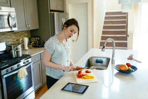 Woman using digital tablet and chopping food in domestic kitchen