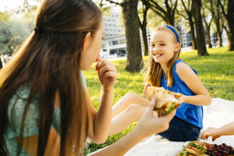 Smiling Caucasian sisters eating food at picnic