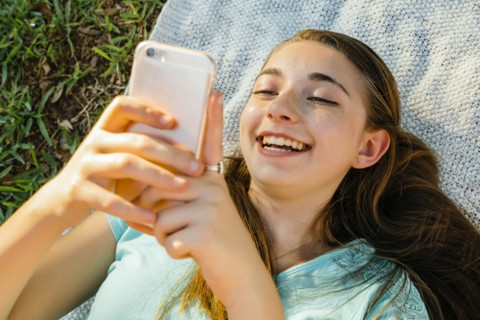 Laughing Caucasian girl laying on blanket texting on cell phone