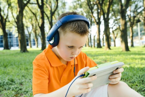 Serious Caucasian boy listening to digital tablet in park