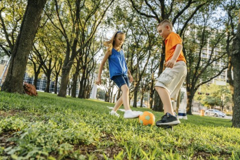 Caucasian brother and sister kicking soccer ball in park
