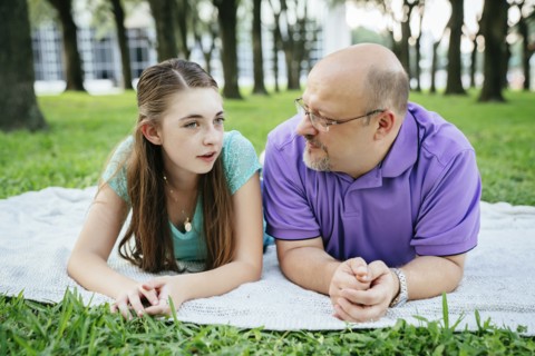 Serious Caucasian father and daughter talking on blanket in park