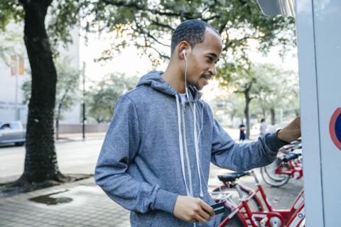 Black man with earbuds paying for bicycle rental with credit card