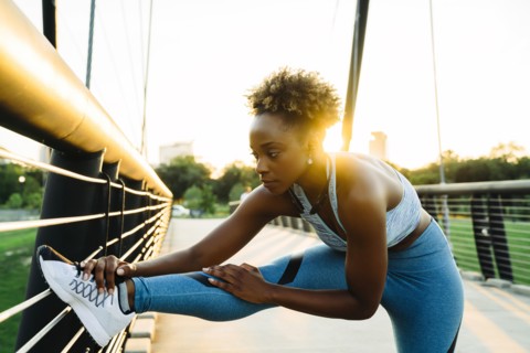 Mixed race woman stretching leg on bridge railing