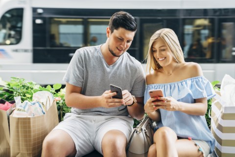 Caucasian couple with shopping bags texting on cell phones near train
