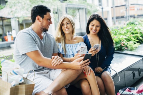 Friends sitting on bench texting on cell phones